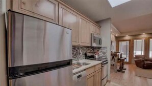 A modern kitchen with stainless steel appliances, wooden cabinets, and a large window.