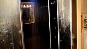 A modern shower with a glass enclosure, a wooden floor, and a ceiling-mounted light fixture.