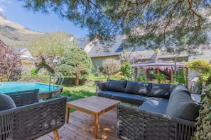 A pool area with a wooden deck, a black sofa, and wicker chairs.