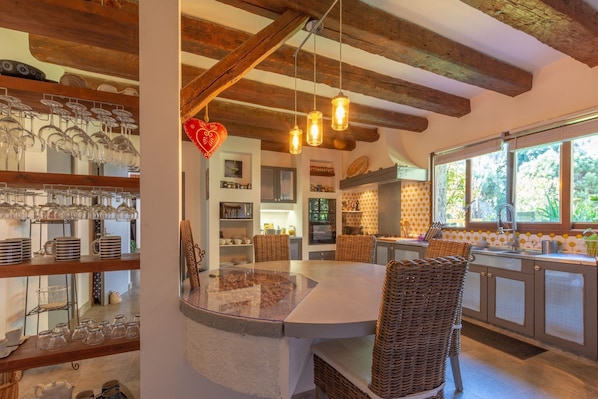 A kitchen with a central island, hanging pendant lights, and a window with a view of greenery.