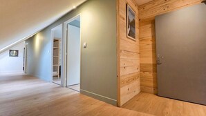 Un couloir doté d’un plancher en bois, une porte fermée et un tableau accroché au mur.