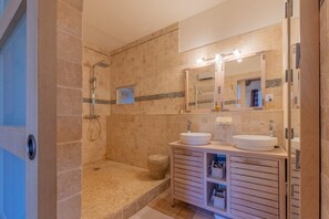 Ein modernes Badezimmer mit begehbarer Dusche, zwei Waschbecken und einem großen Spiegel.