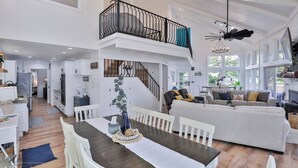 Ein geräumiger Wohnbereich mit hoher Decke, einer Treppe zu einem Balkon und einem Essbereich mit Tisch und Stühlen.