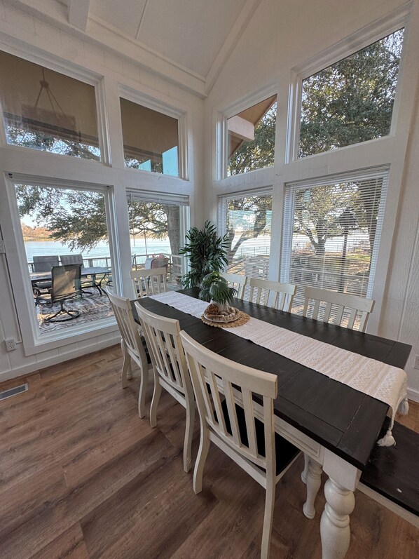 A dining area with a long table, white chairs, and large windows overlooking a body of water.