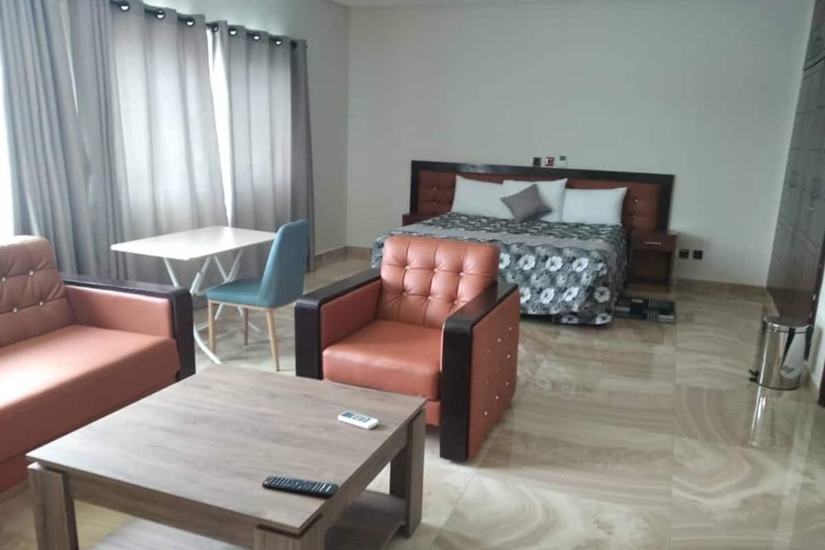 A hotel room with a bed, a sofa, a chair, a small table, and a nightstand.