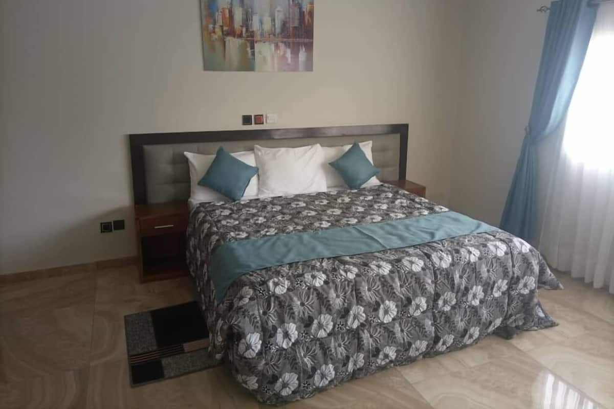 A neatly arranged bedroom with a large bed, a nightstand, a wall-mounted painting, and a window with curtains.