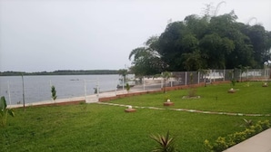 Un espacio verde con vista a un cuerpo de agua, un sendero cercado y un árbol grande.