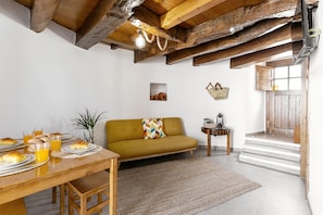 A cozy living room with a wooden dining table set for breakfast, a sofa, and a staircase leading to an upper floor.