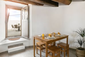 A dining area with a wooden table set for four, a bench, and a view through an open door to an outdoor seating area.