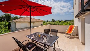 Un balcon avec une table, des chaises, un parasol rouge et une chaise sur laquelle est posée une serviette.