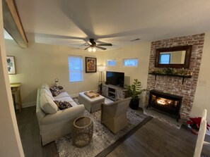 Ein Wohnzimmer mit Sofa, Couchtisch, Fernseher, Kamin und Deckenventilator.