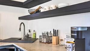 Een moderne keuken met een marmeren aanrecht, een koffiezetapparaat en keukengerei op planken.