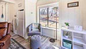 Een moderne woonkamer met een bruine leren bank, een grijze fauteuil en een rond houten poefje. Een witte boekenkast met een 'wifi'-bordje is zichtbaar, en een 'CABIN'-bord hangt aan de muur.