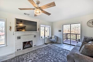 Una sala de estar con chimenea, ventilador de techo, ventana grande y un sofá.