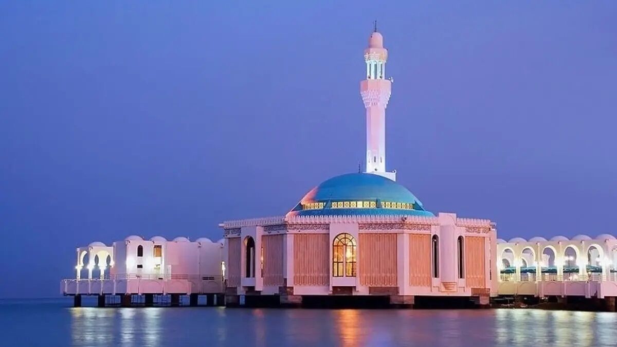 A mosque with a prominent minaret and a large dome, situated on stilts over water.