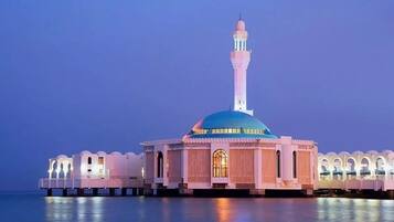 A mosque with a prominent minaret and a large dome, situated on stilts over water.