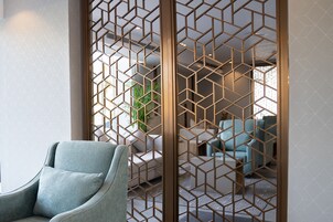 A modern living room with a geometric patterned partition, a light blue armchair, and a sofa with light blue cushions.