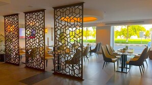 A modern dining area with high tables and chairs, partitioned by geometric screens, and large windows offering a view of the outdoors.
