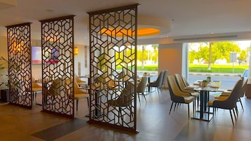 A modern dining area with high tables and chairs, partitioned by geometric screens, and large windows offering a view of the outdoors.
