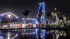 A nighttime cityscape with illuminated buildings, a reflective pool, and a statue of a horse.