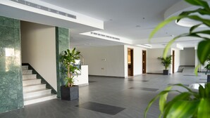 A spacious lobby with a marble staircase, potted plants, and a modern ceiling design.
