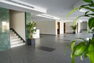 A spacious lobby with a marble staircase, potted plants, and a modern ceiling design.