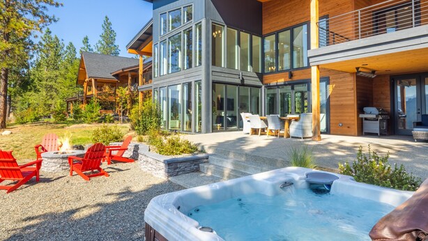 Een modern herenhuis met twee verdiepingen, grote ramen, een jacuzzi, buitenmeubels en een vuurplaats.