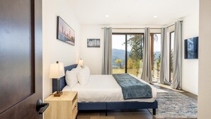 Een slaapkamer met een bed, nachtkastjes, en uitzicht op het omliggende landschap, met een raam voorzien van gordijnen.
