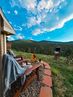 A wooden deck with a bench and a guitar, a barbecue grill, and a view of a forested mountain range. - SALT WATER HOT TUB at Rabbit Hole A Frame In the Woods (Conifer)