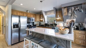 A modern kitchen with a large island, stainless steel appliances, wooden cabinets, and pendant lighting.