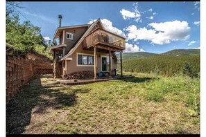 A two-story house with a wooden balcony, a brick wall on the left, and a grassy yard. - SALT WATER HOT TUB at Rabbit Hole A Frame In the Woods (Conifer)