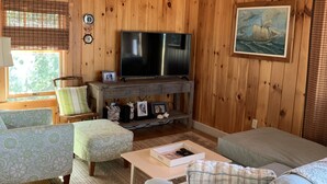 Tunnelmallinen, puinen mökki, jonka sisustuksessa on televisio, pehmustetut istuimet ja seinällä taulu.