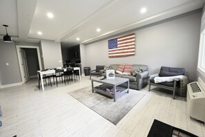 A modern living room with a grey sofa, a coffee table, and a dining area with a white table and chairs.