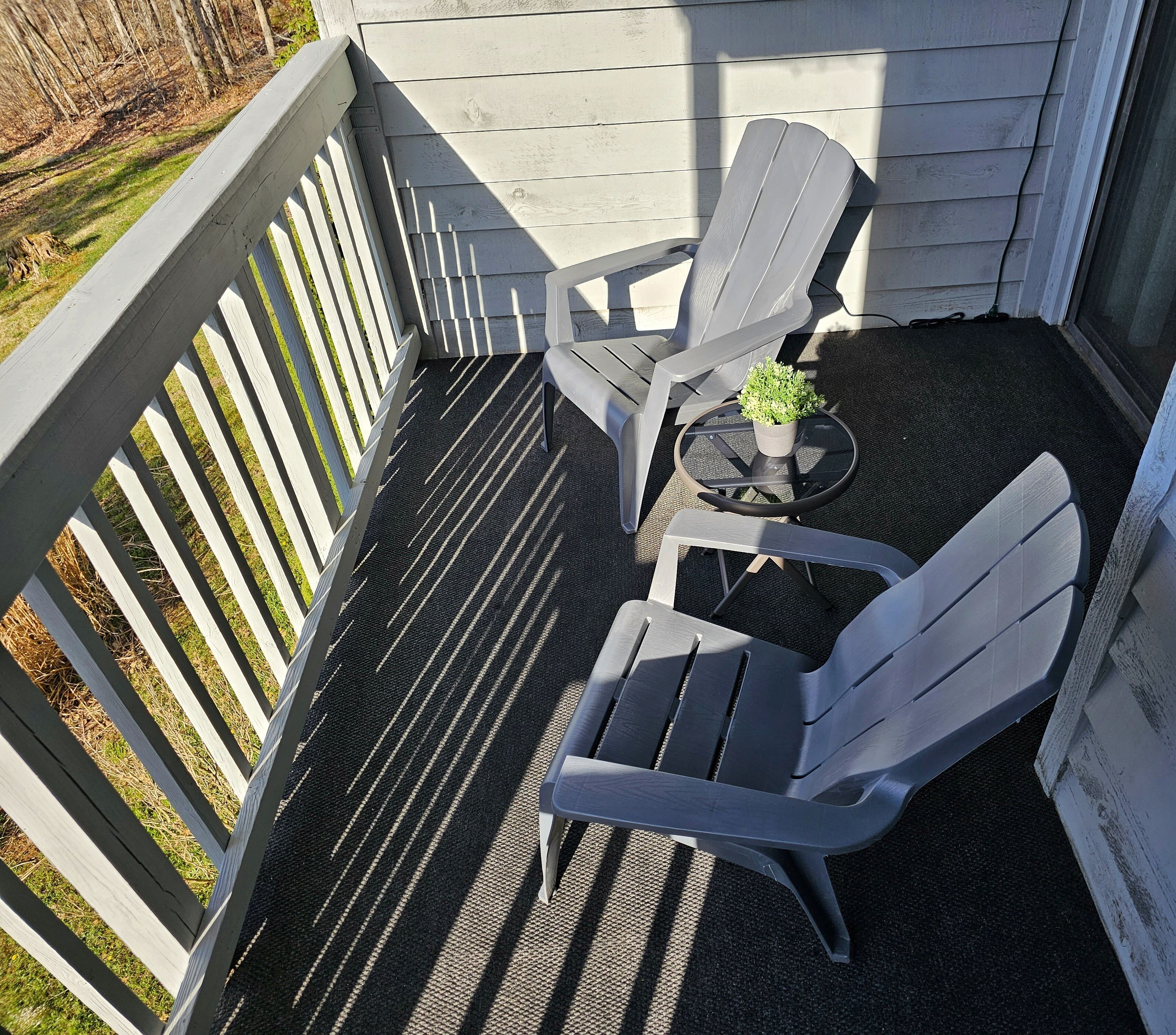 Une petite terrasse extérieure avec deux fauteuils Adirondack et une petite table ronde agrémentée d’une plante en pot.