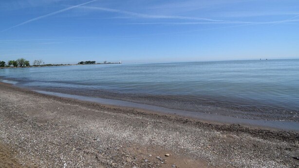 A beach with a pebbly shore and calm water extending to the horizon. - NickelPlate Beach House w Street Legal Golf Cart (Huron)
