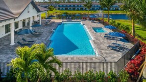 A swimming pool with lounge chairs and umbrellas, surrounded by a landscaped garden and a building with a tiled roof. - Cozy new construction townhome.  (Naples)