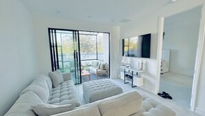 A modern living room with a sectional sofa, a flat-screen TV, and a sliding glass door leading to a balcony. - Cozy new construction townhome.  (Naples)