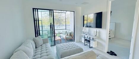 A modern living room with a sectional sofa, a flat-screen TV, and a sliding glass door leading to a balcony.
