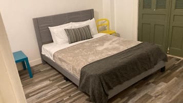 Un dormitorio con cama, mesita de noche, silla y puerta.