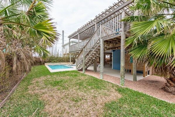 Une terrasse en bois avec un escalier menant à une zone abritée, une piscine et des palmiers.