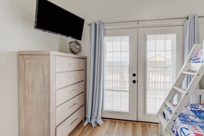 A bedroom with a wooden dresser, a television mounted above it, a bed with a ladder, and a sliding glass door with curtains.