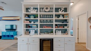 Een keuken met een vast kookeiland, witte kasten en een inbouwkoelkast. Links een blauwe kast en rechts een witte deur.