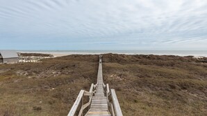 Een houten looppad dat naar een strand leidt, met een gebouw op de achtergrond.