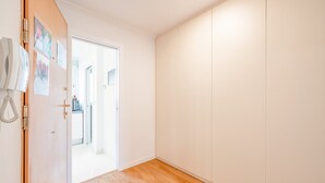 A hallway with a wooden floor, white walls, and a door leading to another room.