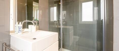 Une salle de bain moderne avec une douche à parois de verre, un lavabo blanc et un grand miroir.