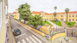 A yellow building with a red roof, a paved courtyard, and a car parked on the street.