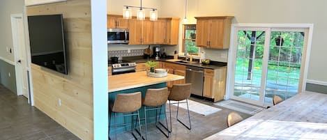 Una cocina moderna con armarios de madera, una isla central con taburetes y un horno empotrado, además de un amplio ventanal con vistas al exterior.