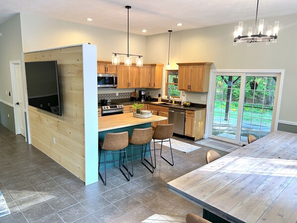 A modern kitchen with wooden cabinets, a central island with bar stools, a built-in oven, and a large window providing a view of the outdoors.