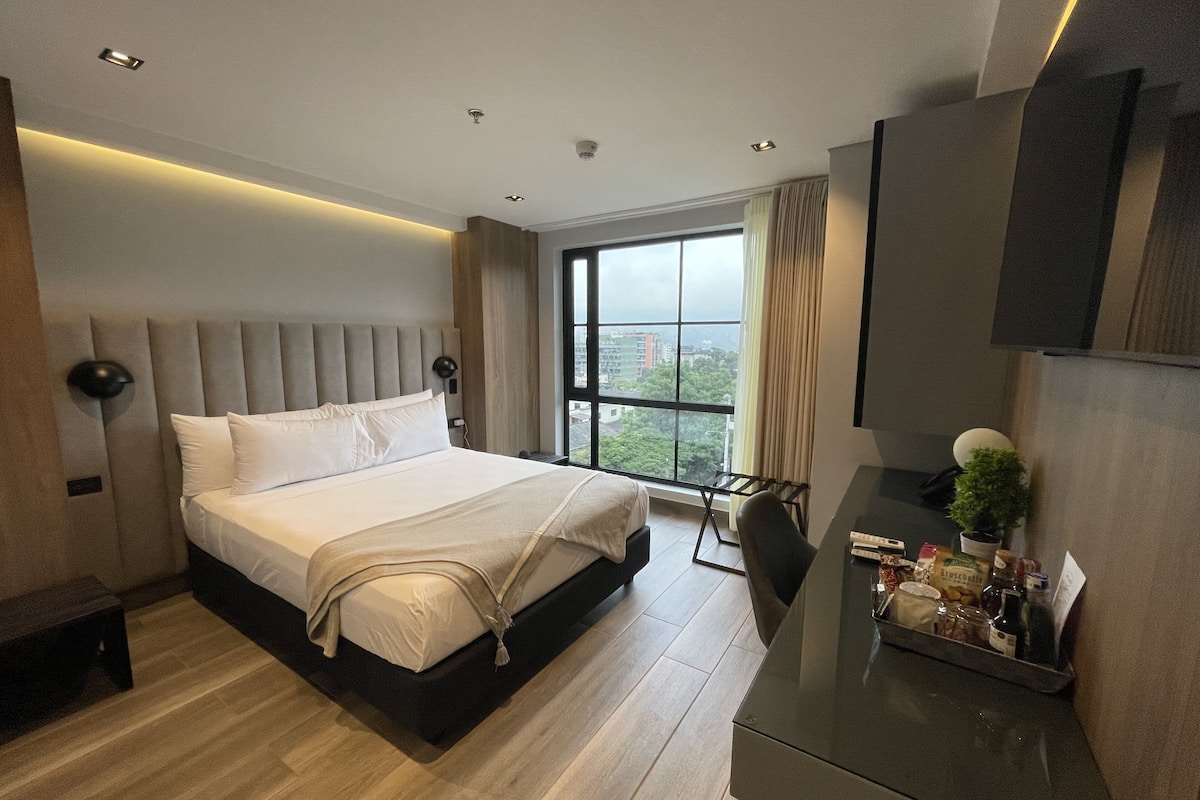 A modern hotel room with a large bed, a desk, and a view of the city.