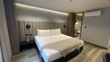 Una habitación de hotel moderna con una cama grande, mesitas de noche, un espejo y un equipo de aire acondicionado integrado.